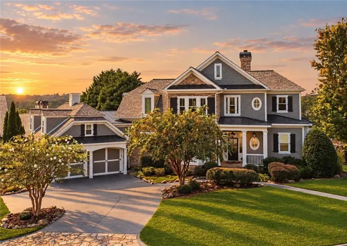 Elegant two-story Colonial with gray exterior siding and white trim, featuring a covered front porch with white columns, circular window detail, and brick chimney