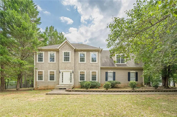 Two-story stucco exterior featuring a prominent gabled entry, multiple double-hung windows, and dormer windows