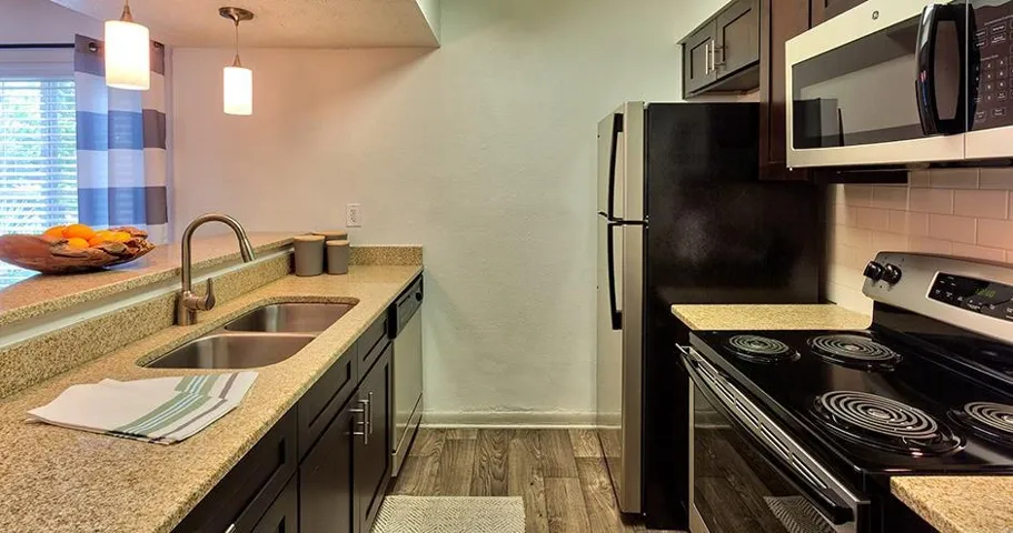 Kitchen featuring wood-finish flooring, dark cabinetry, light-toned countertops, a stainless steel double sink, and pendant lighting