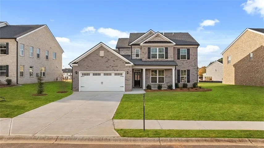 Two-story brick exterior with a gabled roofline, front-facing two-car garage, covered entry, and established landscaping
