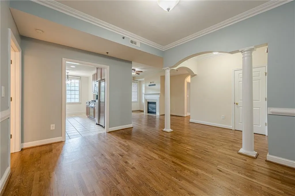 Unfurnished living room with wood finished floors, ornate columns, a fireplace with flush hearth, crown molding, and arched walkways