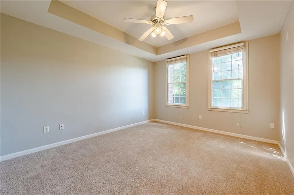 Empty room with a raised ceiling, light carpet, and ceiling fan