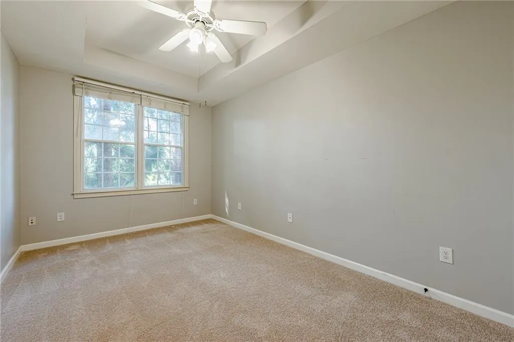 Unfurnished room featuring a tray ceiling, light carpet, and ceiling fan