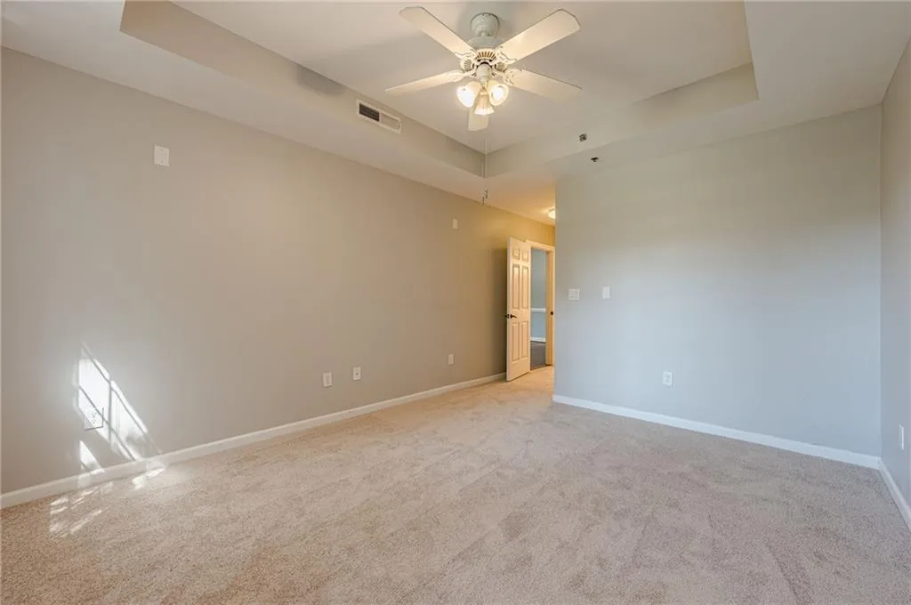 Unfurnished room featuring a raised ceiling, light carpet, and a ceiling fan