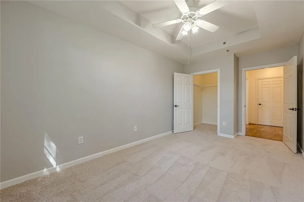 Unfurnished bedroom with light carpet, a tray ceiling, a ceiling fan, and a walk in closet