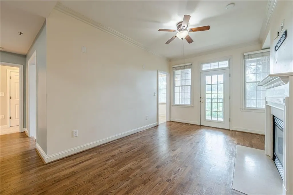 Unfurnished living room featuring a fireplace with flush hearth, ceiling fan, wood finished floors, and crown molding