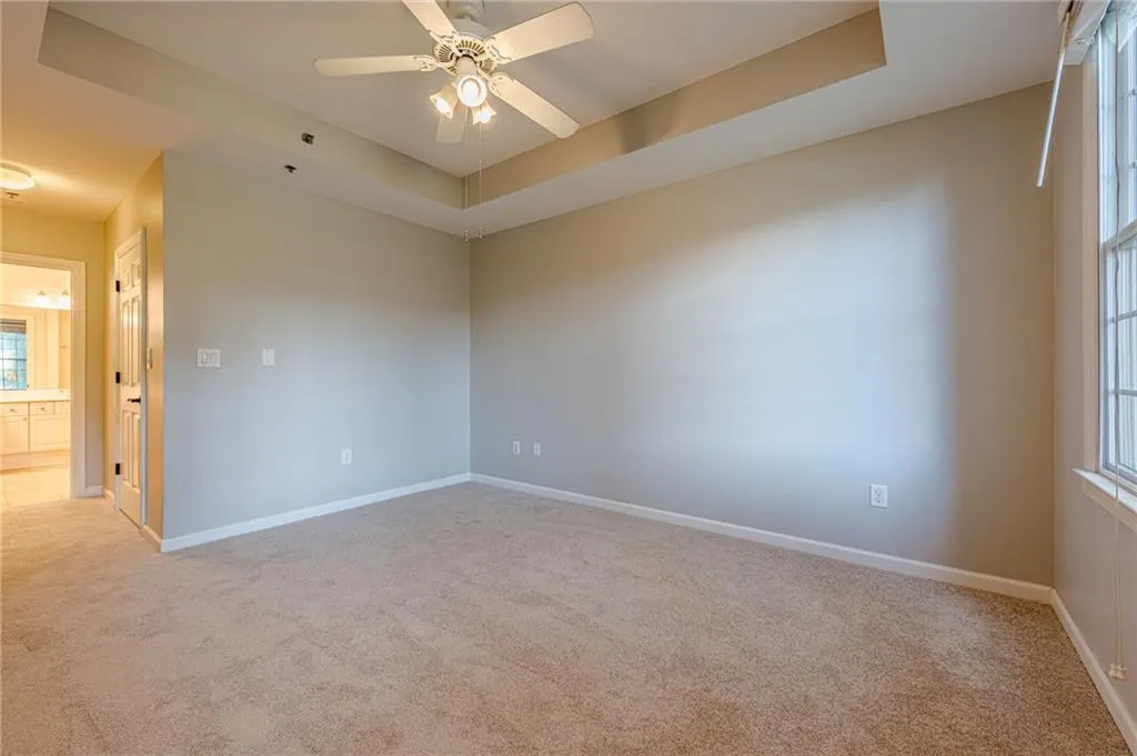 Carpeted spare room featuring a raised ceiling and a ceiling fan