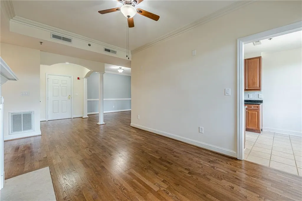 Unfurnished living room featuring ornate columns, ceiling fan, arched walkways, light wood finished floors, and crown molding