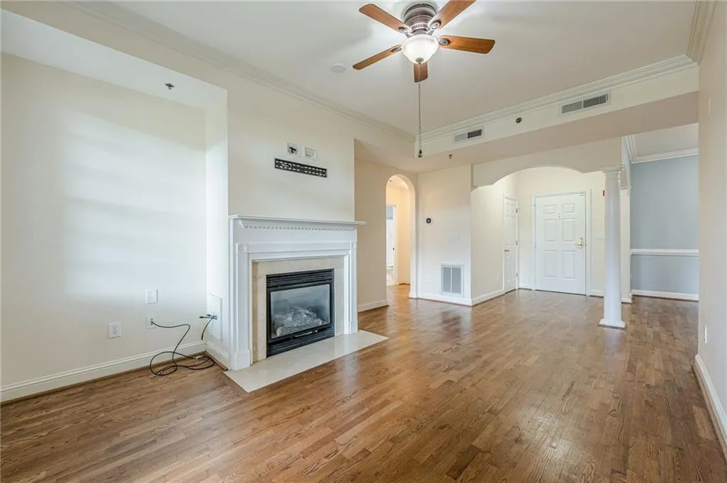 Unfurnished living room featuring a ceiling fan, wood finished floors, a high end fireplace, crown molding, and arched walkways