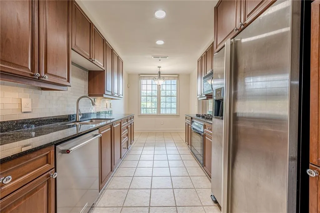 Kitchen featuring stainless steel appliances, decorative backsplash, light tile patterned flooring, decorative light fixtures, and dark stone counters