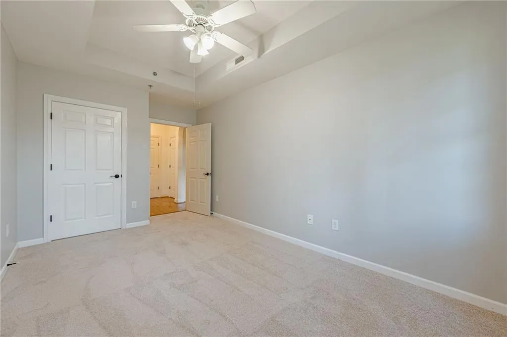 Unfurnished bedroom with light colored carpet, a tray ceiling, and ceiling fan