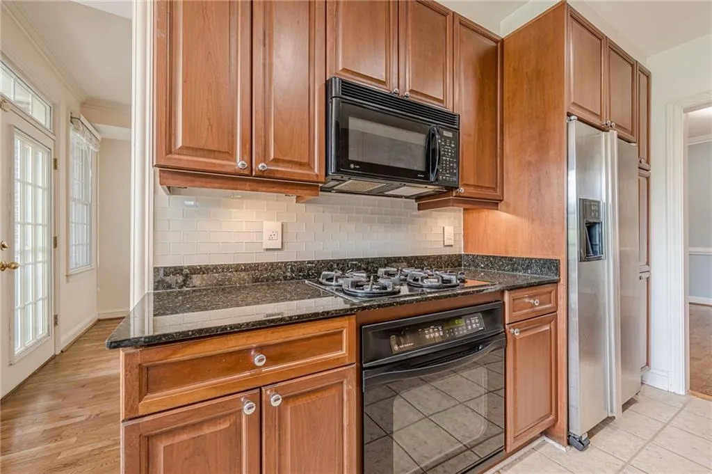 Kitchen featuring black appliances, crown molding, decorative backsplash, dark stone countertops, and brown cabinets
