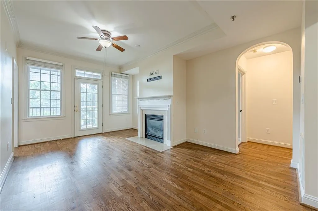 Unfurnished living room featuring ceiling fan, wood finished floors, arched walkways, a fireplace with flush hearth, and ornamental molding