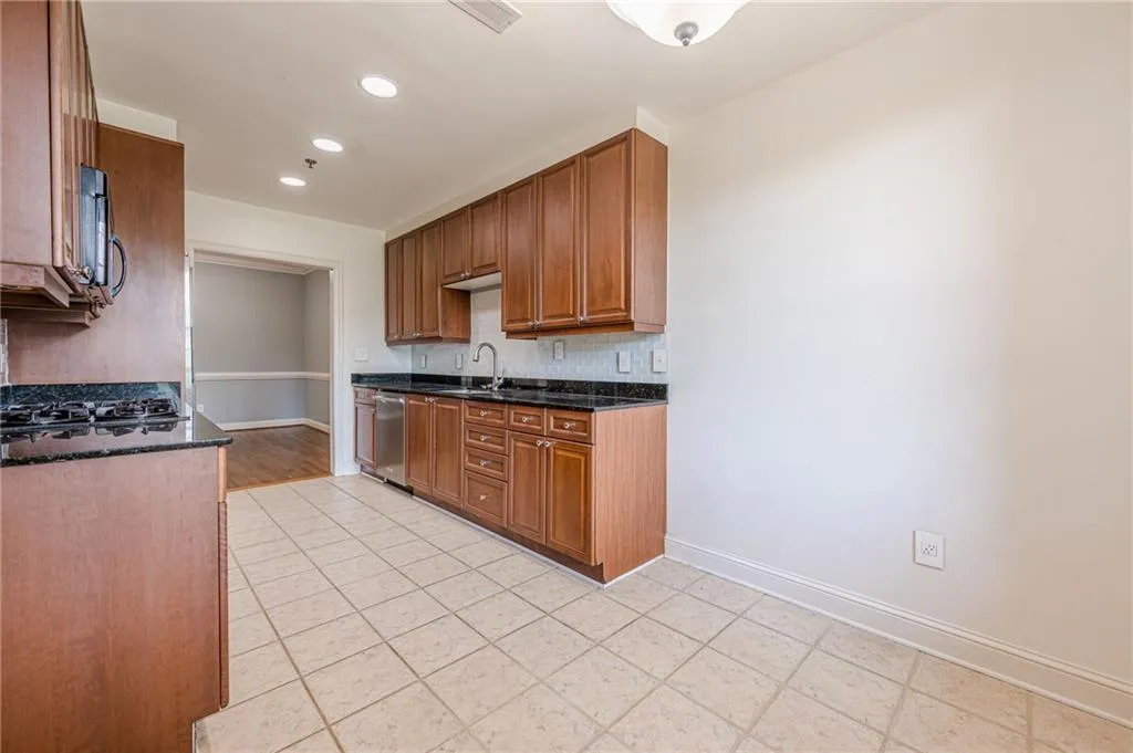 Kitchen with backsplash, recessed lighting, light tile patterned floors, brown cabinets, and dark stone countertops