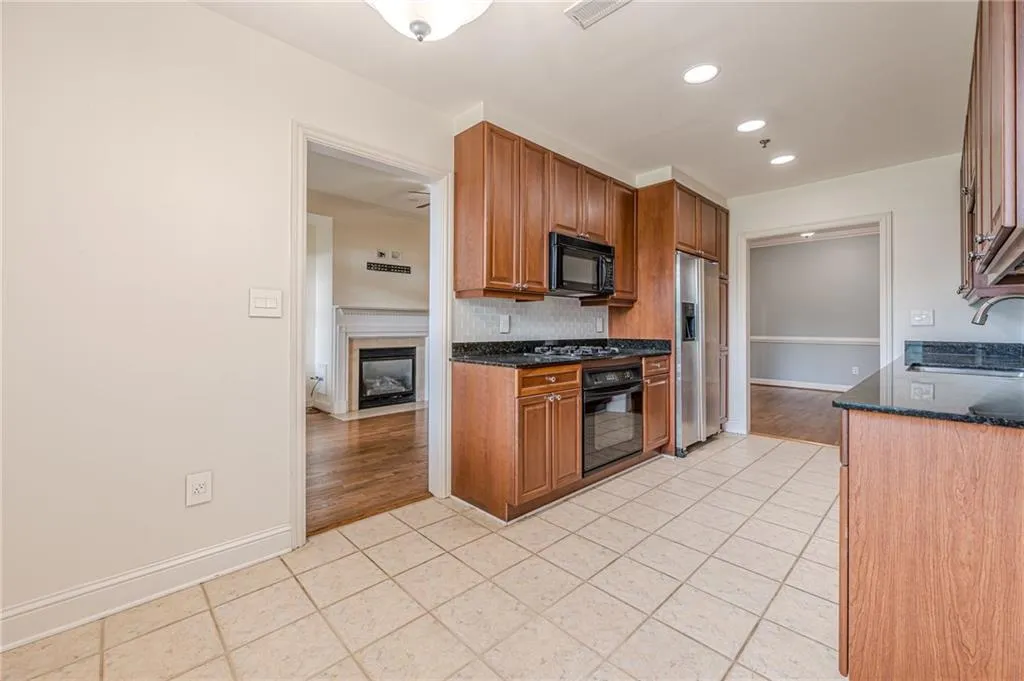 Kitchen featuring light tile patterned floors, black appliances, backsplash, dark stone counters, and recessed lighting
