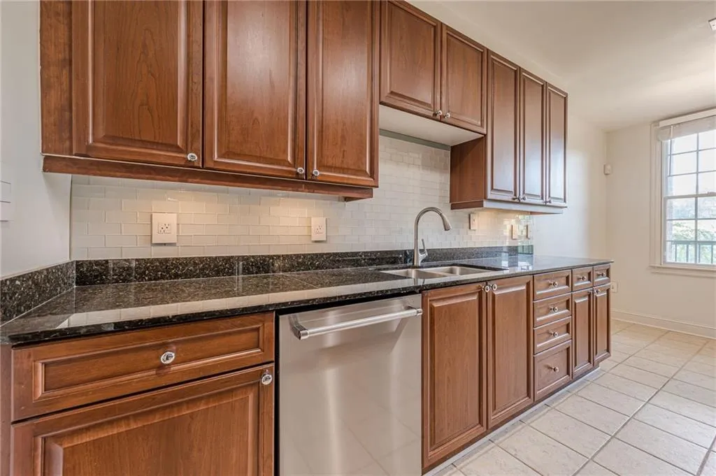 Kitchen with stainless steel dishwasher, decorative backsplash, light tile patterned floors, and dark stone counters
