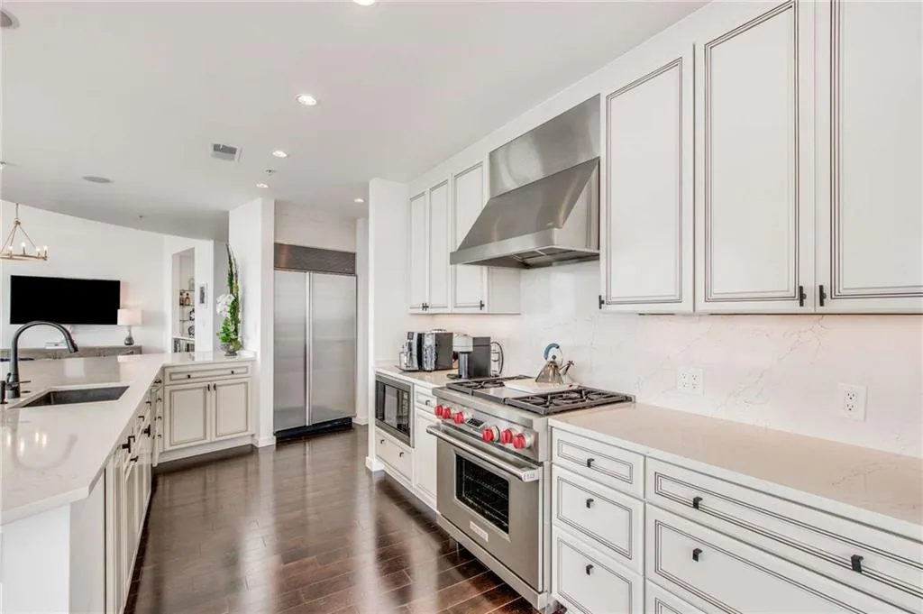 Kitchen featuring light stone countertops, built in appliances, wall chimney range hood, dark wood-type flooring, and a peninsula
