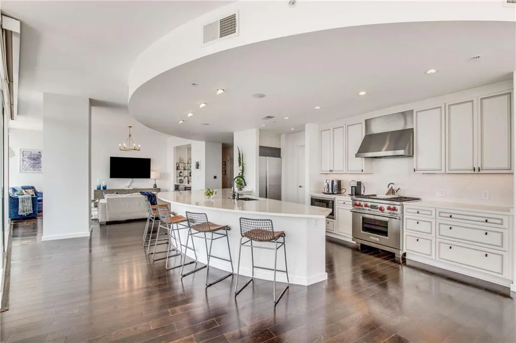 Kitchen featuring appliances with stainless steel finishes, a large island with sink, wall chimney range hood, white cabinets, and open floor plan