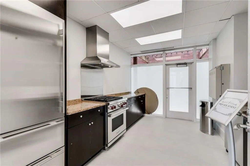 Kitchen with stainless steel appliances, range hood, a paneled ceiling, and light stone countertops