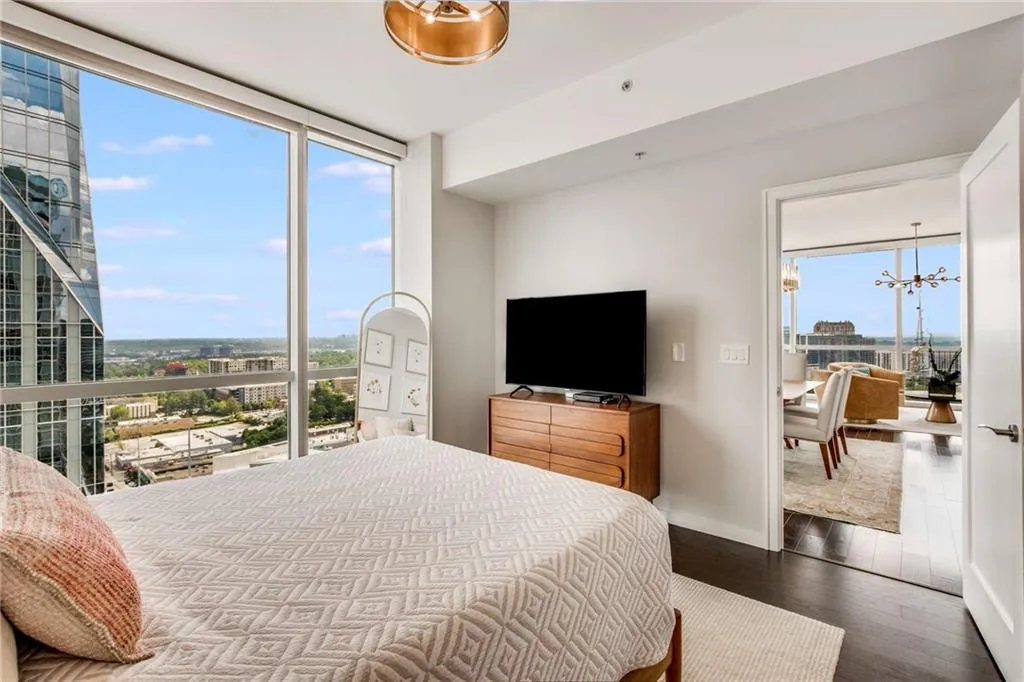 Bedroom with a chandelier, multiple windows, dark wood-style floors, and floor to ceiling windows
