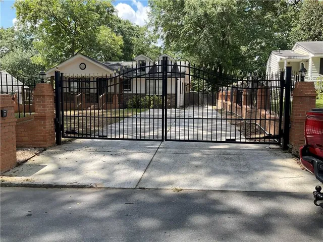 Wrought iron gate with brick pillars, concrete driveway, and mature trees
