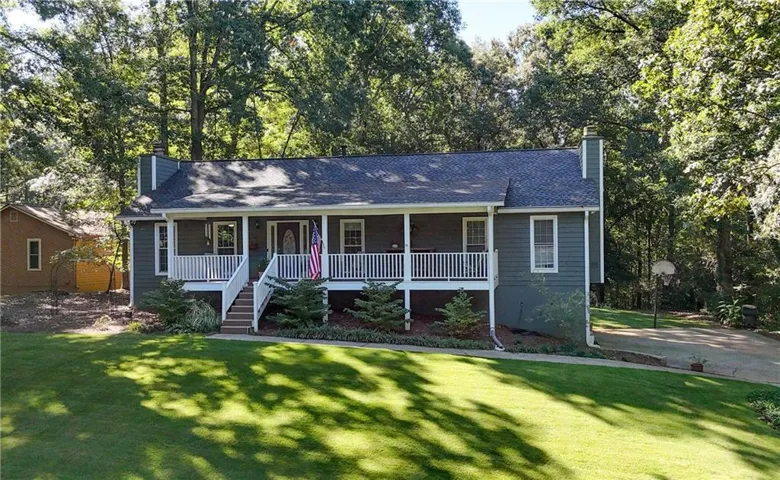 Expansive front lawn with mature trees, a covered porch with white railings, and a side-entry driveway