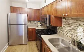 Kitchen featuring stainless steel appliances, decorative backsplash, light countertops, brown cabinetry, and light wood-style flooring