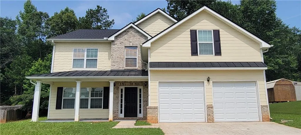Two-story residence featuring light yellow siding, a two-car garage, and a covered front porch with white columns