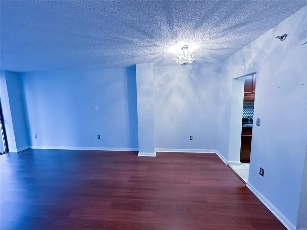 Unfurnished room with dark wood-style floors, a textured ceiling, and a chandelier