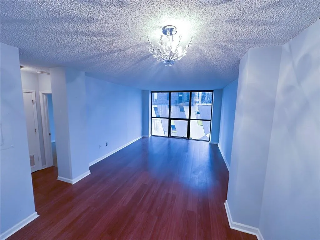 Empty room featuring a wall of windows, dark wood-style flooring, a textured ceiling, and a chandelier