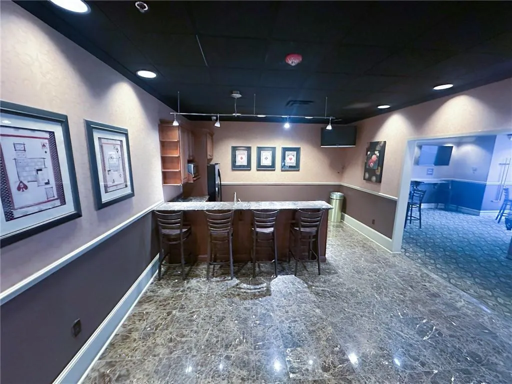 Indoor wet bar with freestanding refrigerator, open shelves, a textured wall, and light stone counters