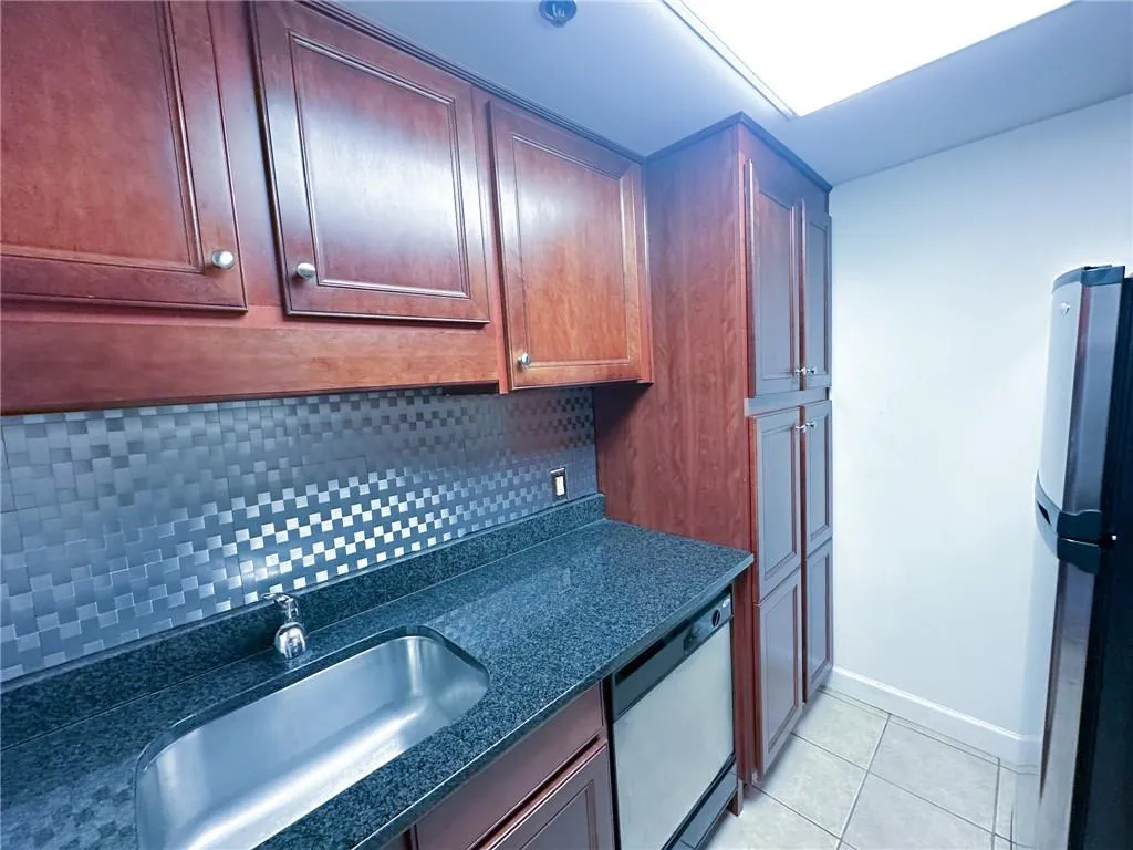 Kitchen featuring freestanding refrigerator, tasteful backsplash, dishwasher, light tile patterned flooring, and dark stone countertops