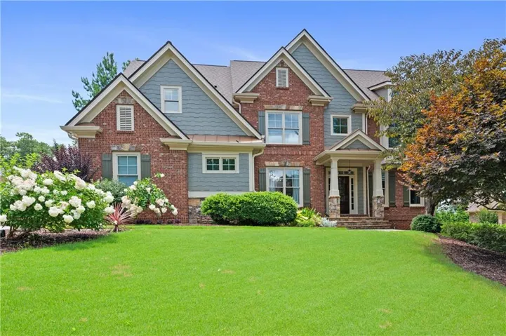 Front elevation showing the brick and fiber cement facade, gabled rooflines, covered front porch with stone columns, and manicured landscaping.