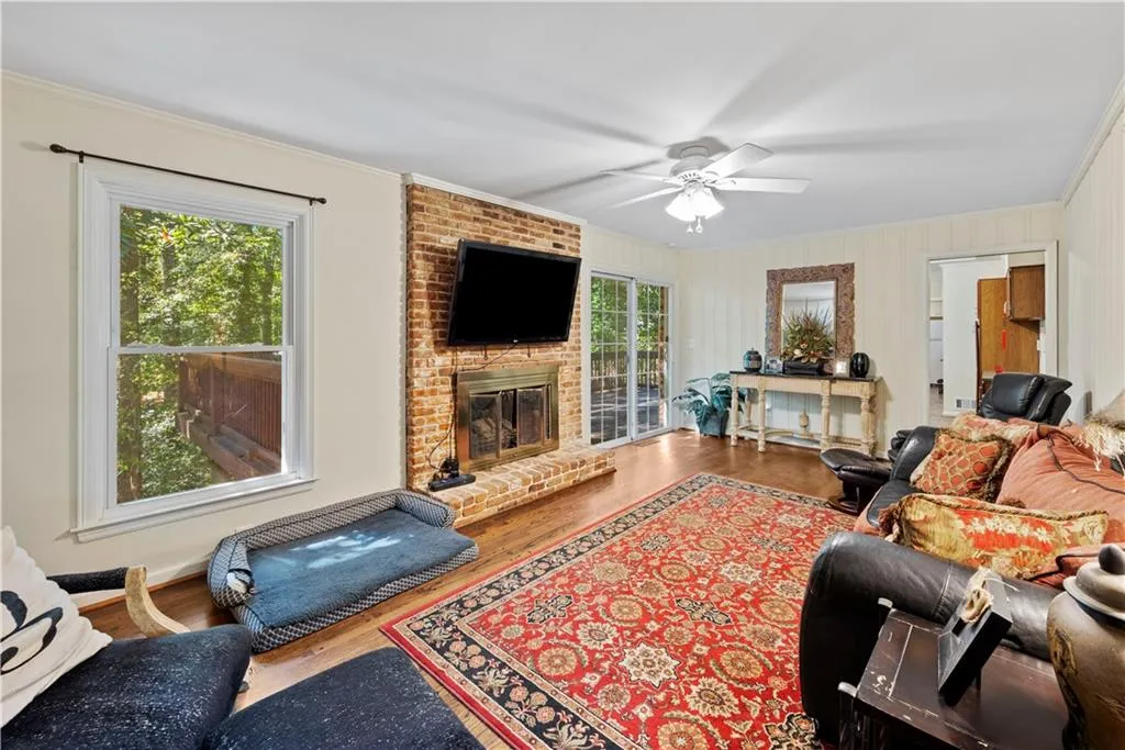 Living area with ornamental molding, wood finished floors, a brick fireplace, and ceiling fan