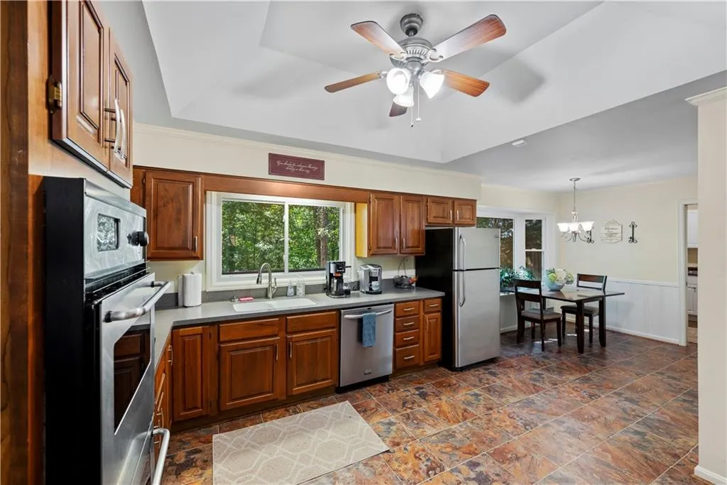 Kitchen featuring stainless steel appliances, brown cabinetry, a ceiling fan, a chandelier, and decorative light fixtures