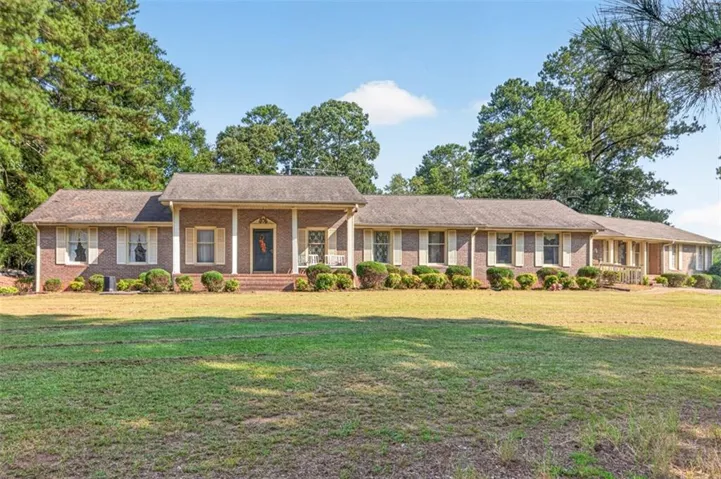 Brick exterior with white shutters, a welcoming front porch with white columns, and a mature tree-lined perimeter