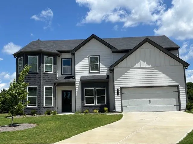 View of front of home featuring board and batten siding, concrete driveway, a front lawn, and roof with shingles