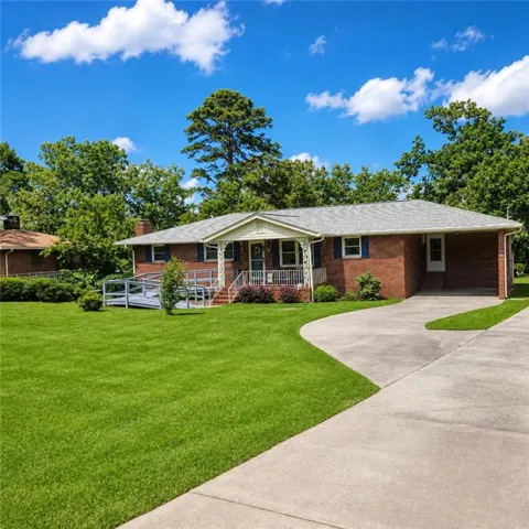 Brick ranch home featuring a covered front porch, curved concrete driveway, and manicured lawn with mature landscaping