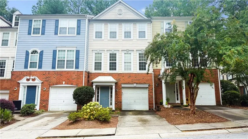 Brick and siding exterior with multiple garage entrances, individual driveways, and mature landscaping