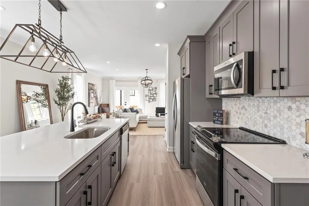 Kitchen with gray cabinetry, appliances with stainless steel finishes, a center island with sink, open floor plan, and recessed lighting