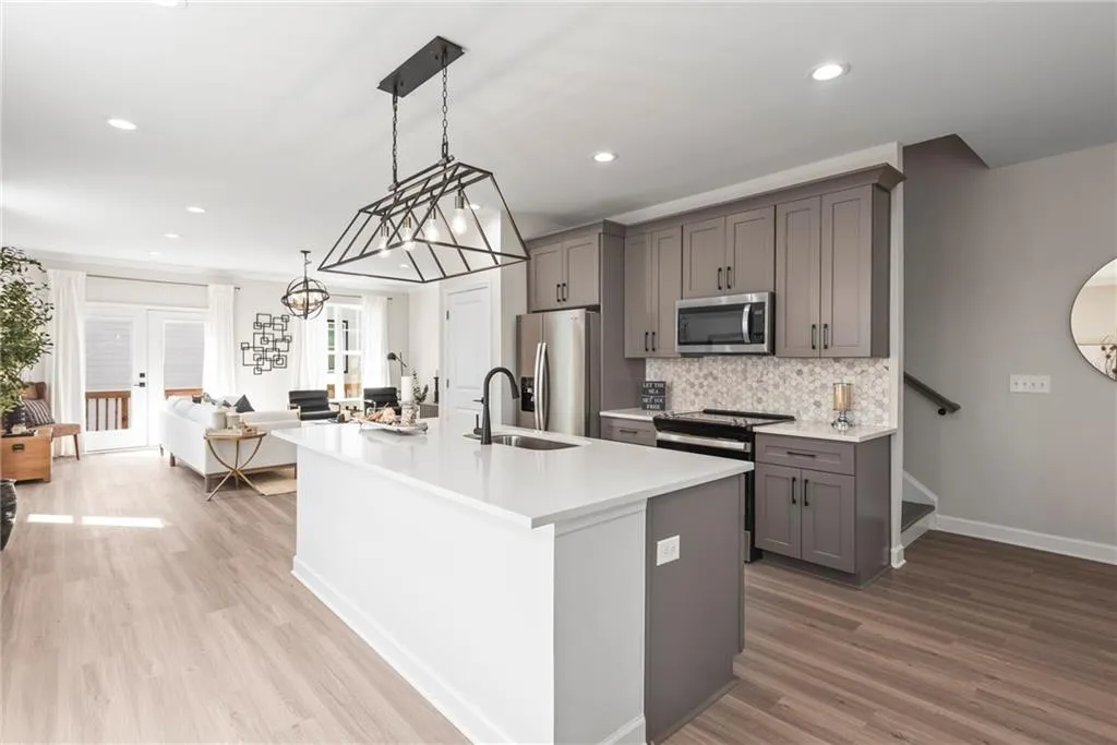 Kitchen featuring pendant lighting, stainless steel appliances, gray cabinetry, an island with sink, and open floor plan