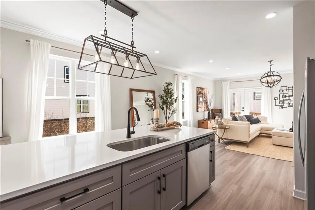 Kitchen with decorative light fixtures, light wood-style floors, appliances with stainless steel finishes, open floor plan, and ornamental molding