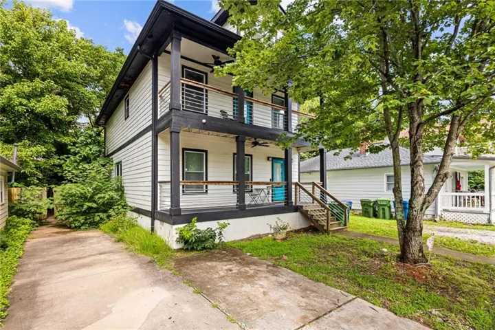 Two-story residence featuring white siding with dark trim, dual-level covered porches with metal railings, and a prominent turquoise entry door