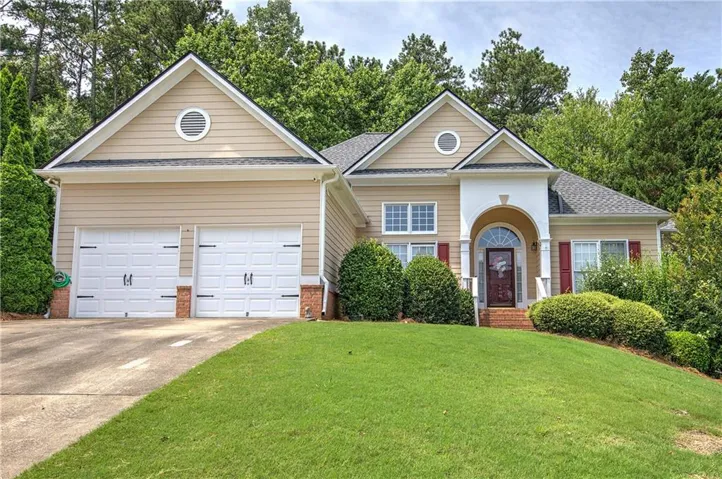 Exterior featuring a two-car garage, arched entry with columns, red shutters, and a sloped lawn