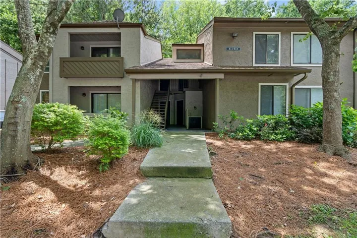 Stucco exterior with multiple balconies, a concrete walkway, and surrounding foliage