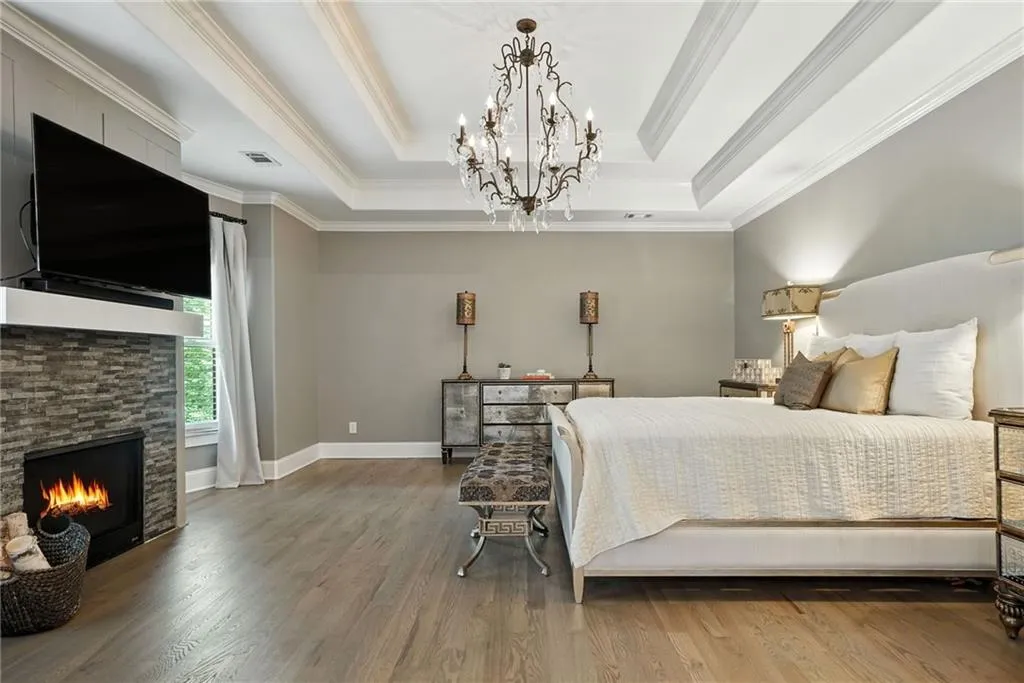 Bedroom with a tray ceiling, wood finished floors, a fireplace, and ornamental molding