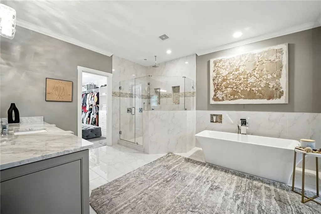 Full bath with a soaking tub, a marble finish shower, vanity, ornamental molding, and a walk in closet