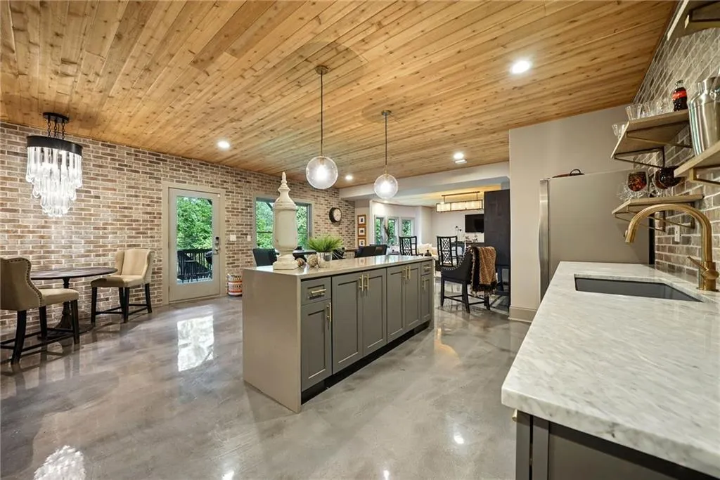 Kitchen featuring brick wall, gray cabinets, light stone counters, open shelves, and recessed lighting