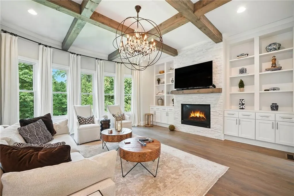 Living area featuring dark wood-style floors, a fireplace, beamed ceiling, a chandelier, and built in features