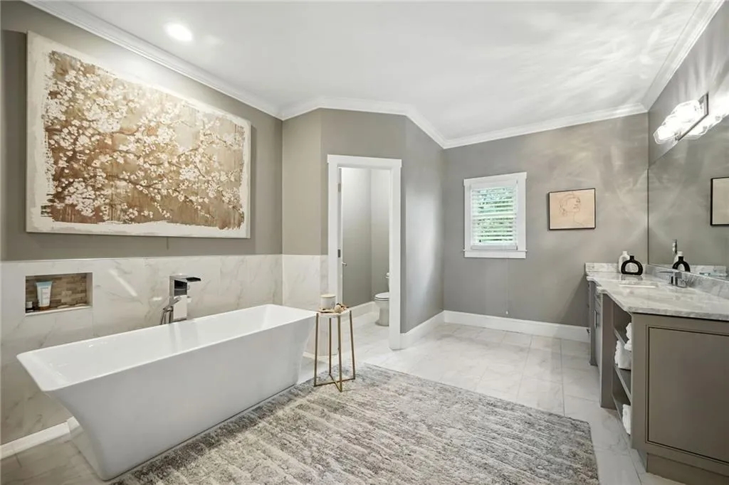 Full bath with vanity, light marble finish flooring, ornamental molding, and a freestanding bath